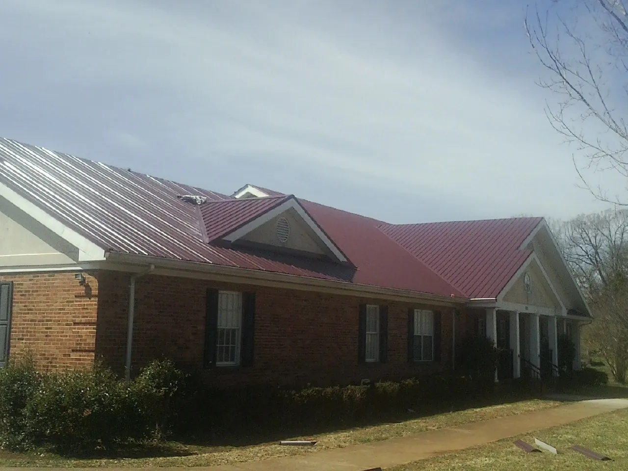 Red metal roof with gabled entries on a long brick building, from a Hail Damage Roof Repair job in Brookhaven