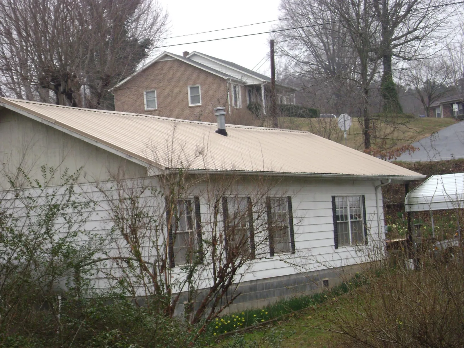 Tan metal roof on a white sided house set into a hillside — Commercial Roofing by Roofing Brothers in Brookhaven