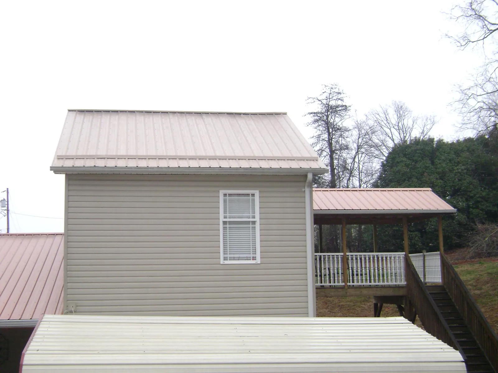 Tan metal roofs on a two story addition and attached porch, from a Roof Replacement job in Brookhaven